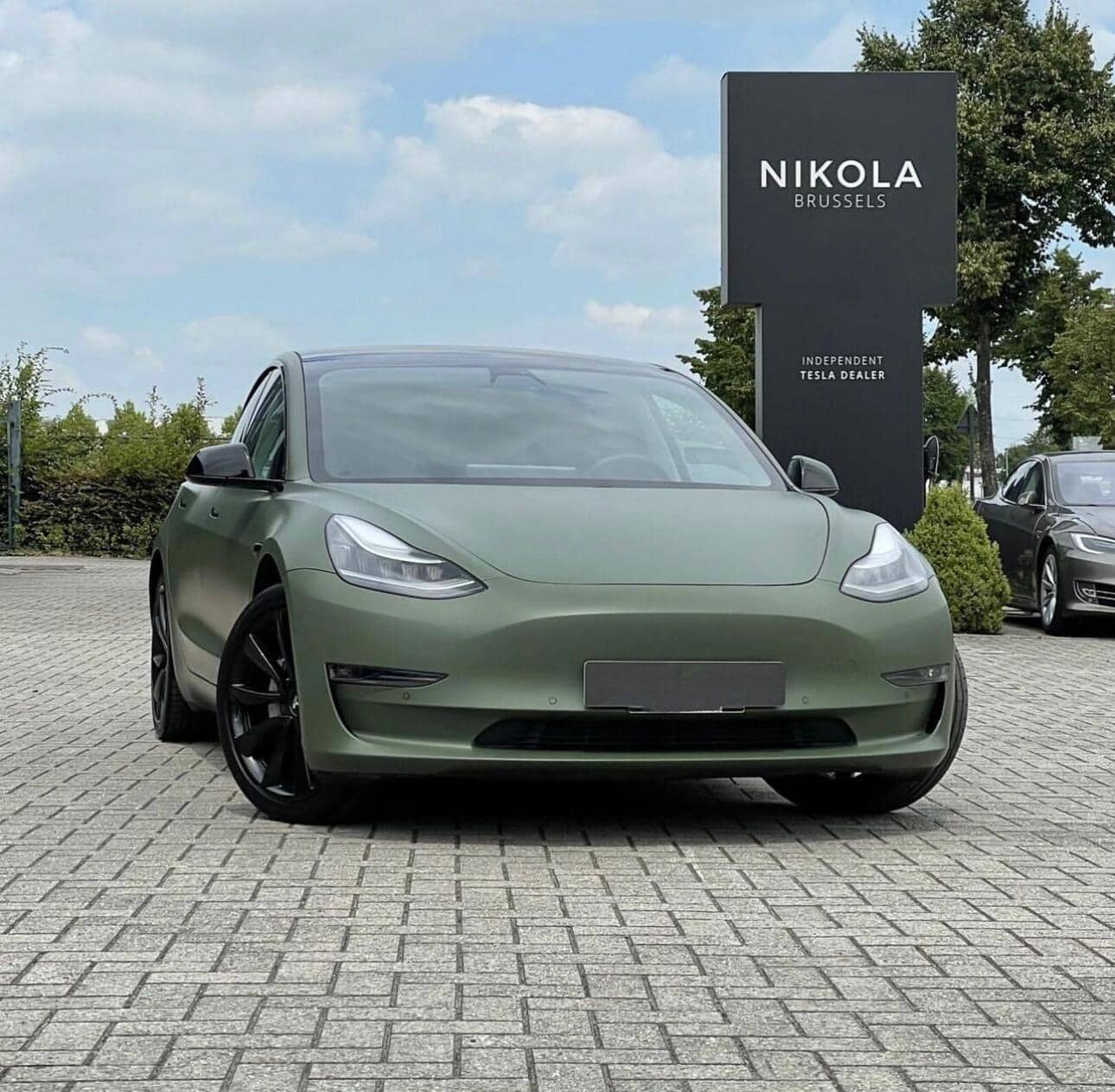 Matte green Tesla Model 3 with black wheels parked in front of Nikola Brussels Tesla dealer