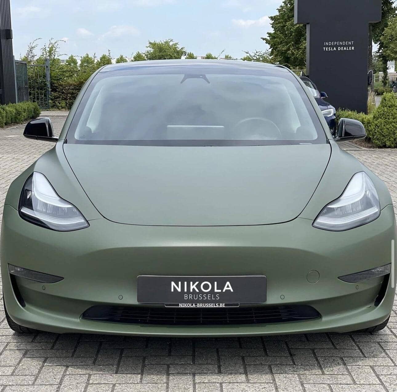 Matte green Tesla Model 3 electric car front view parked outside Nikola Brussels dealership