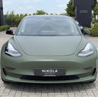 Matte green Tesla Model 3 electric car front view parked outside Nikola Brussels dealership