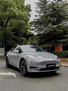 Gray Tesla Model Y with a smooth finish using WrapBug Pre-cut Tesla Vinyl Wrap Kit parked near trees