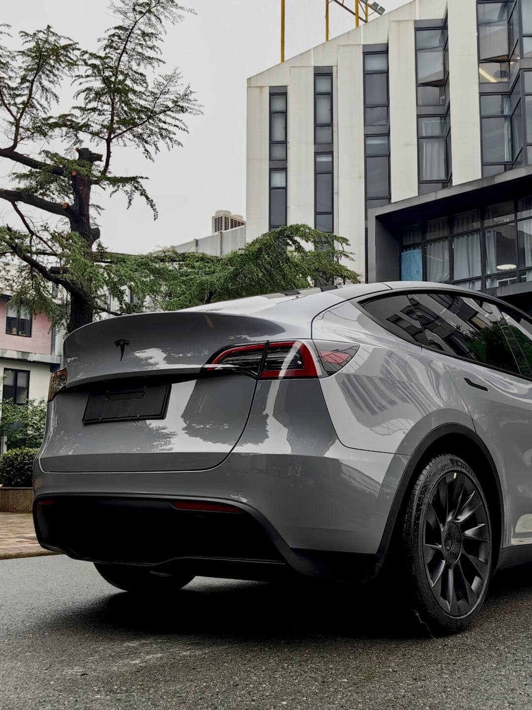 Gray Tesla Model Y parked near buildings showcasing Pre-cut Tesla Vinyl Wrap Kit application on the rear and side