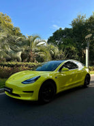 Yellow Tesla car wrapped using Pre-cut Tesla Vinyl Wrap Kit parked outdoors near palm trees