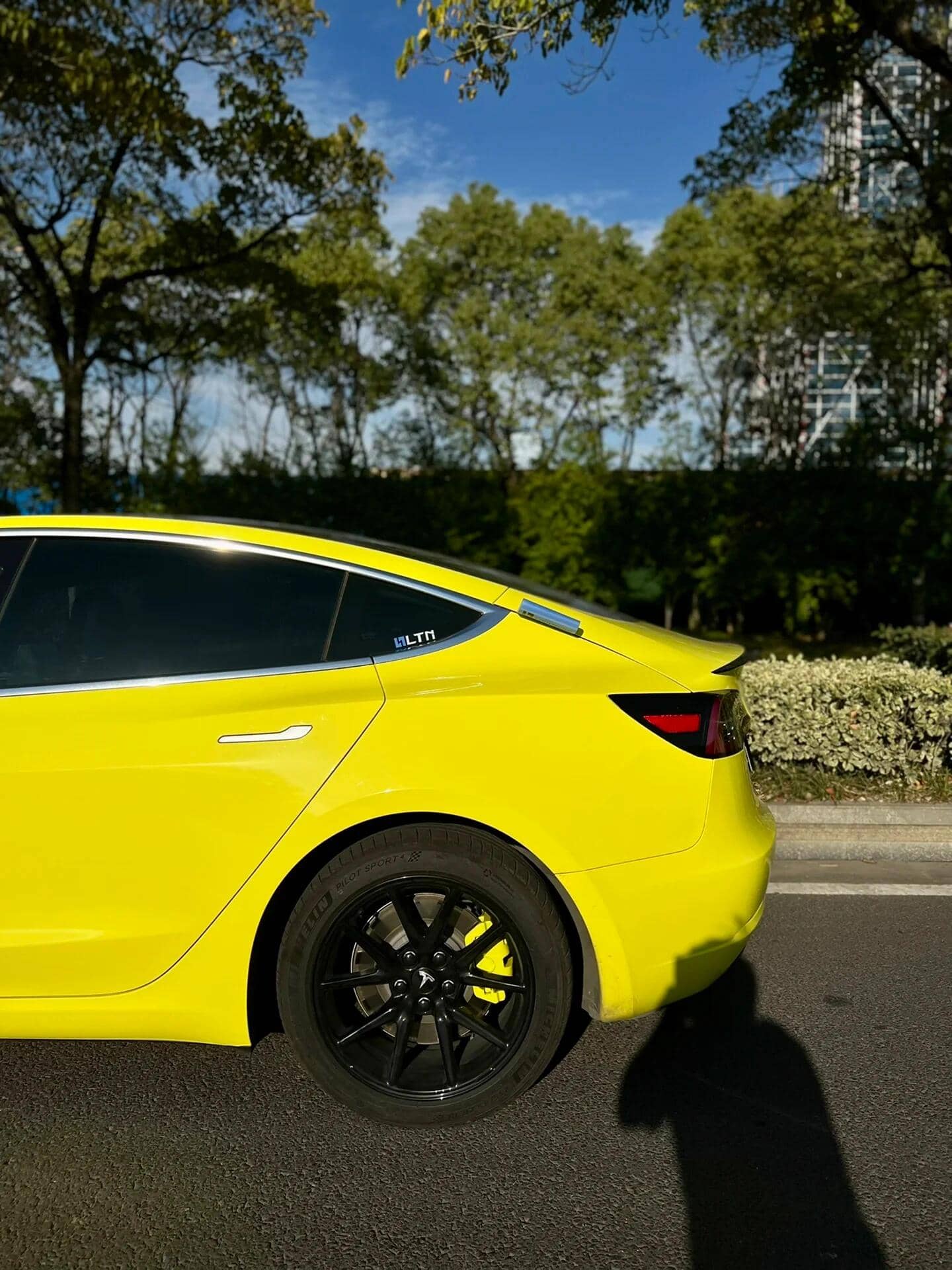 Yellow Tesla Model 3 wrapped using Pre-cut Tesla Vinyl Wrap Kit by WrapBug with black wheels in outdoor setting