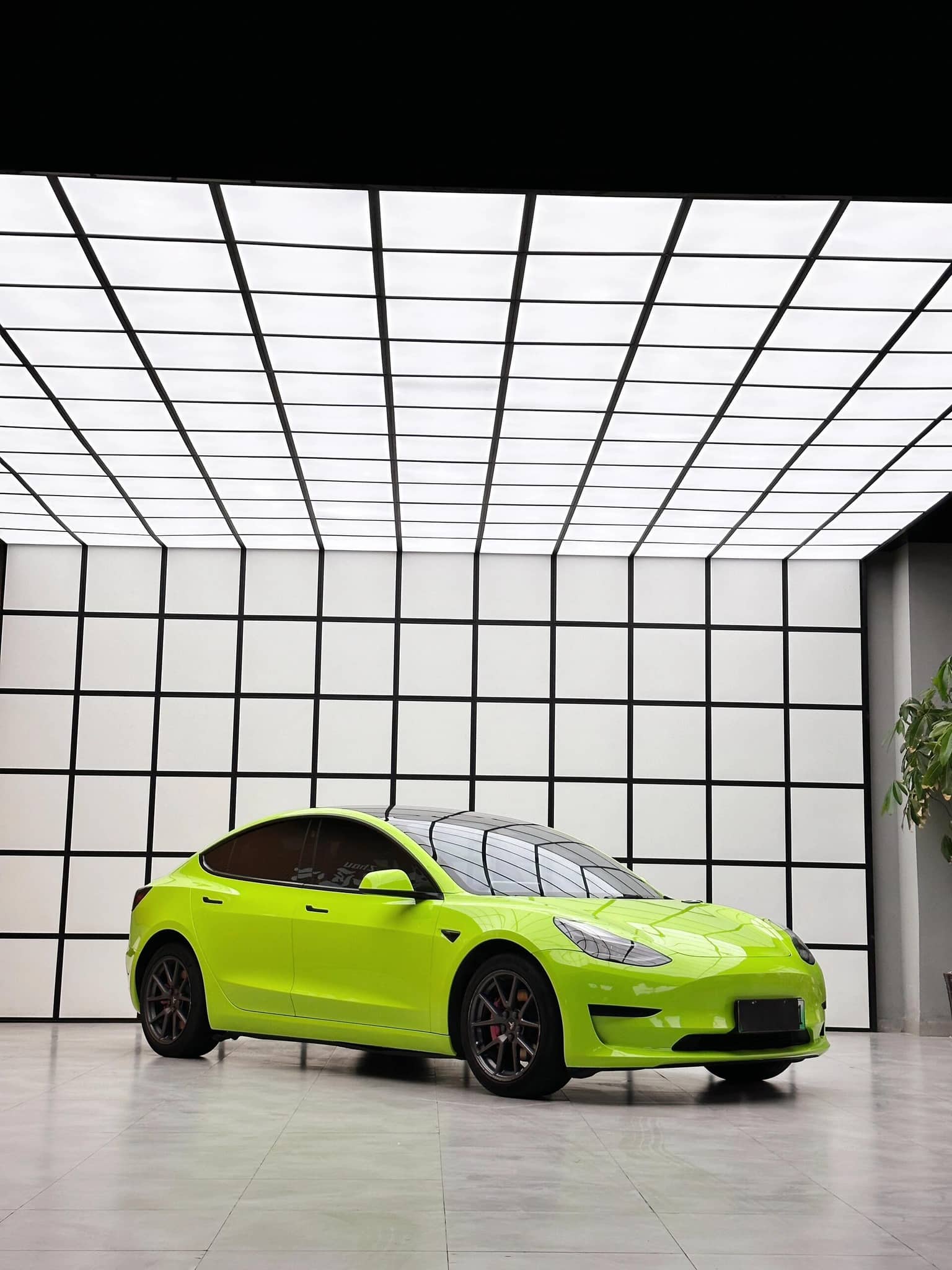 Bright lime green Tesla Model 3 with Pre-cut Tesla Wrap Kit installed in a modern showroom