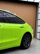 Bright green Tesla Model 3 wrapped with a Pre-cut Tesla Wrap Kit showing rear side view in a modern garage