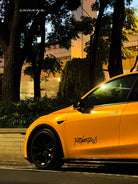 Yellow Tesla car featuring a Pre-cut Tesla Wrap Kit by WrapBug parked at night near trees and buildings