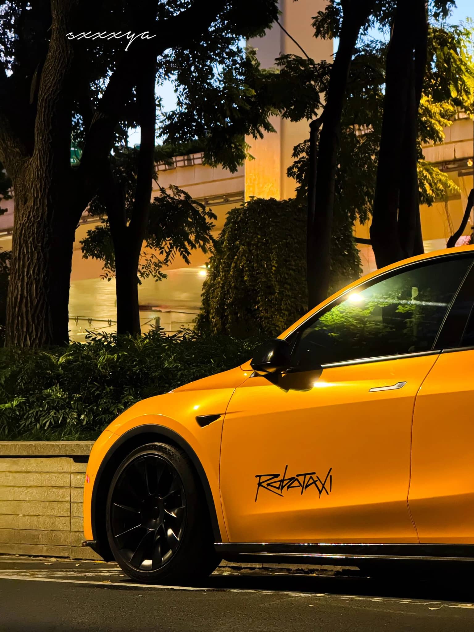 Yellow Tesla car featuring a Pre-cut Tesla Wrap Kit by WrapBug parked at night near trees and buildings