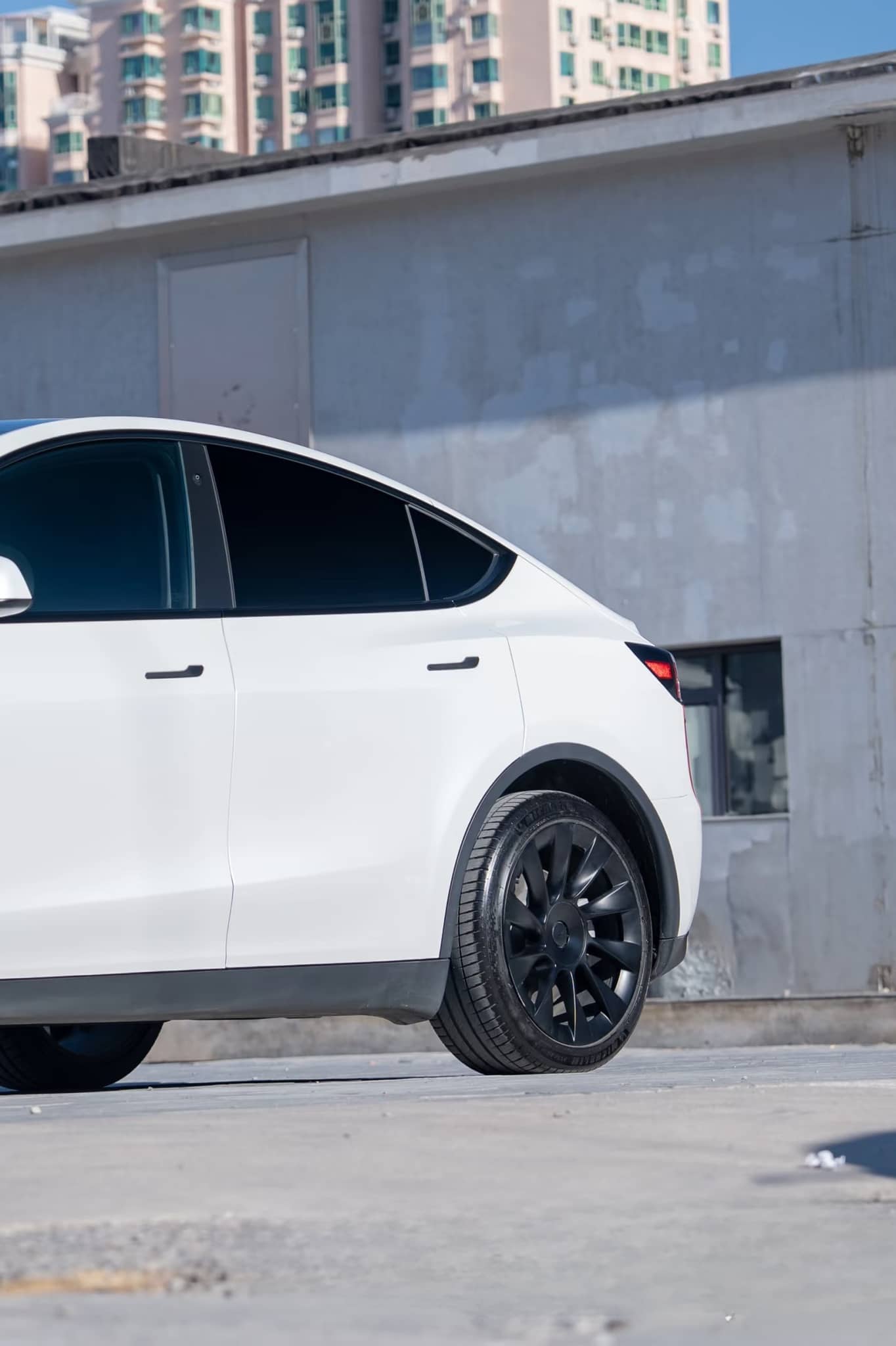 White Tesla Model Y with black wheels featuring a pre-cut Tesla wrap kit by WrapBug on a city street