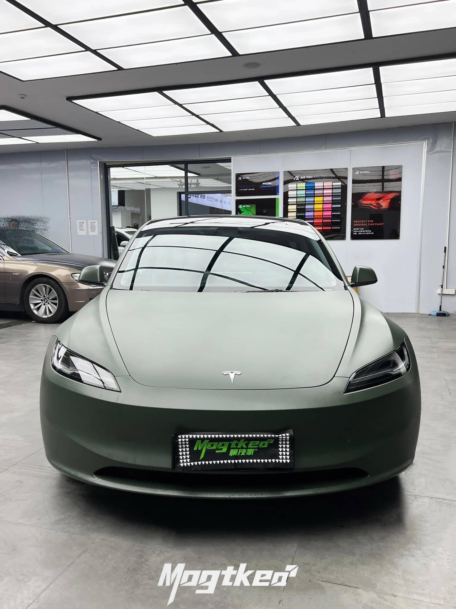 Front view of a Tesla car wrapped in matte OLIVE GREEN tesla wrap inside a modern showroom