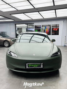 Front view of a Tesla car wrapped in matte OLIVE GREEN tesla wrap inside a modern showroom