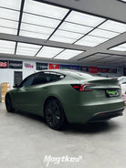 Matte olive green Tesla wrap on a sleek Tesla Model 3 parked inside a garage
