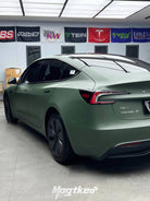 Tesla Model 3 with matte OLIVE GREEN tesla wrap by WrapBug parked indoors with branded banners