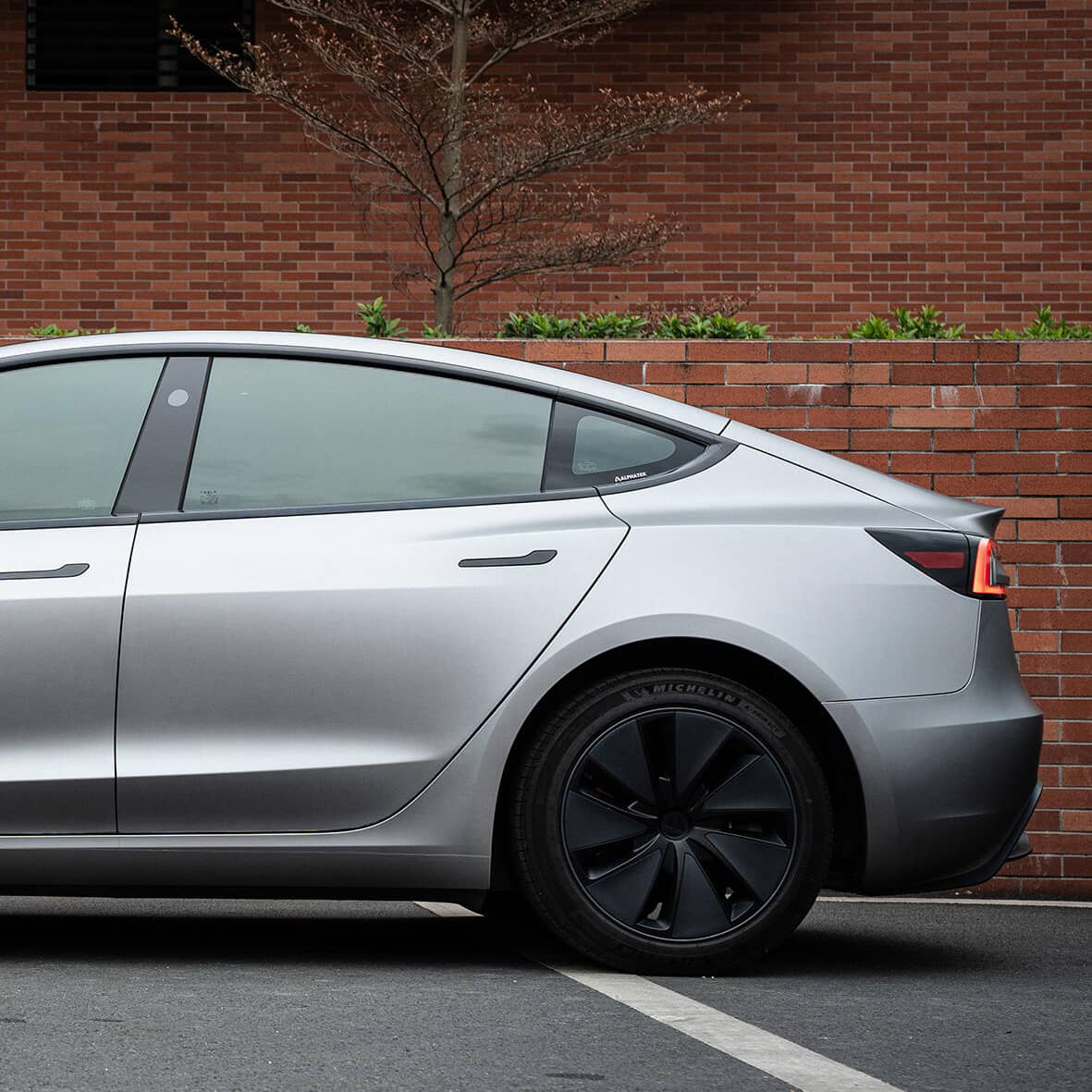 Silver Tesla Model 3 with matte finish parked beside brick wall featuring tesla model 3 wrap