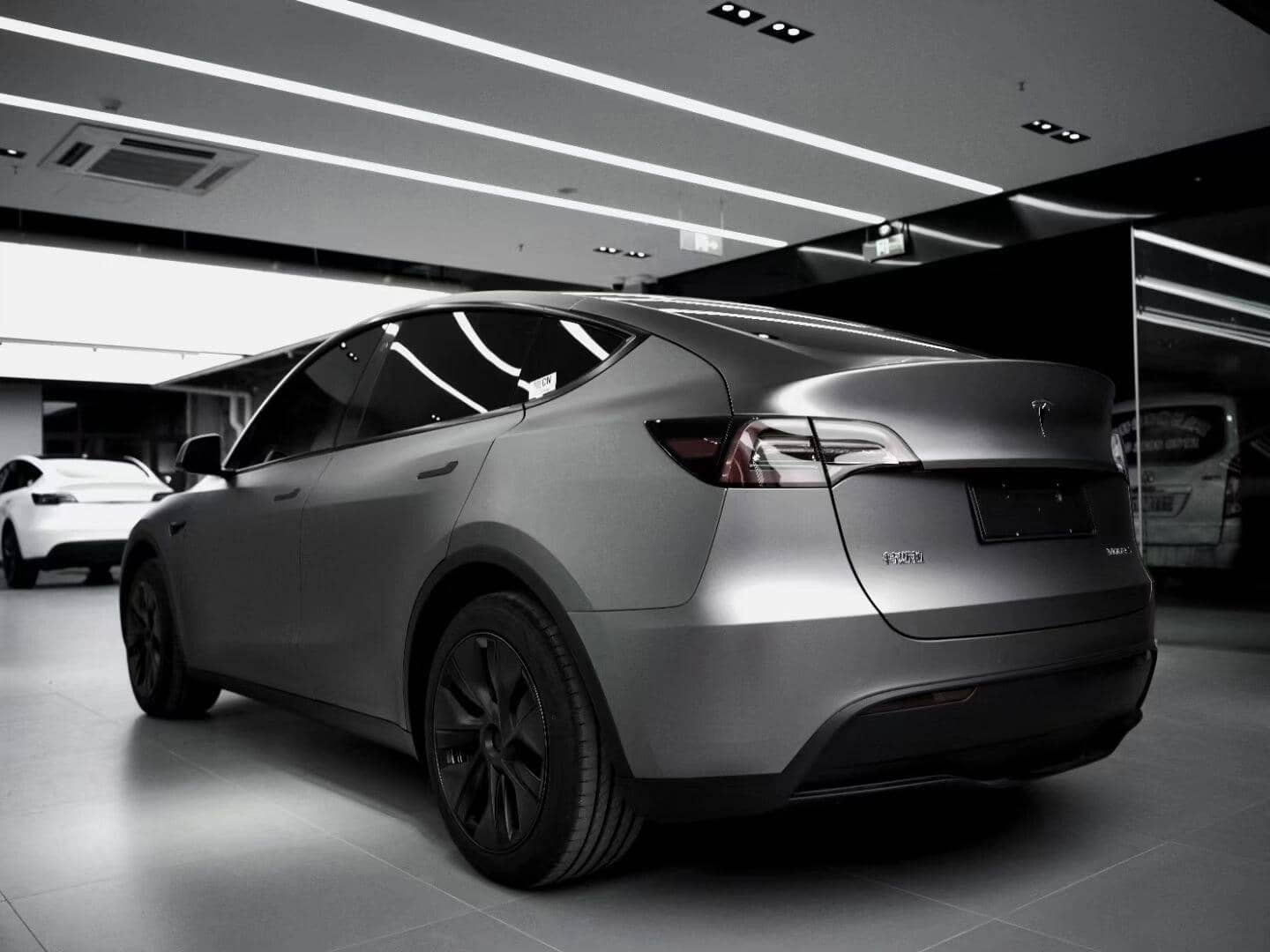 Tesla Model Y electric car in matte gray finish parked indoors under bright ceiling lights