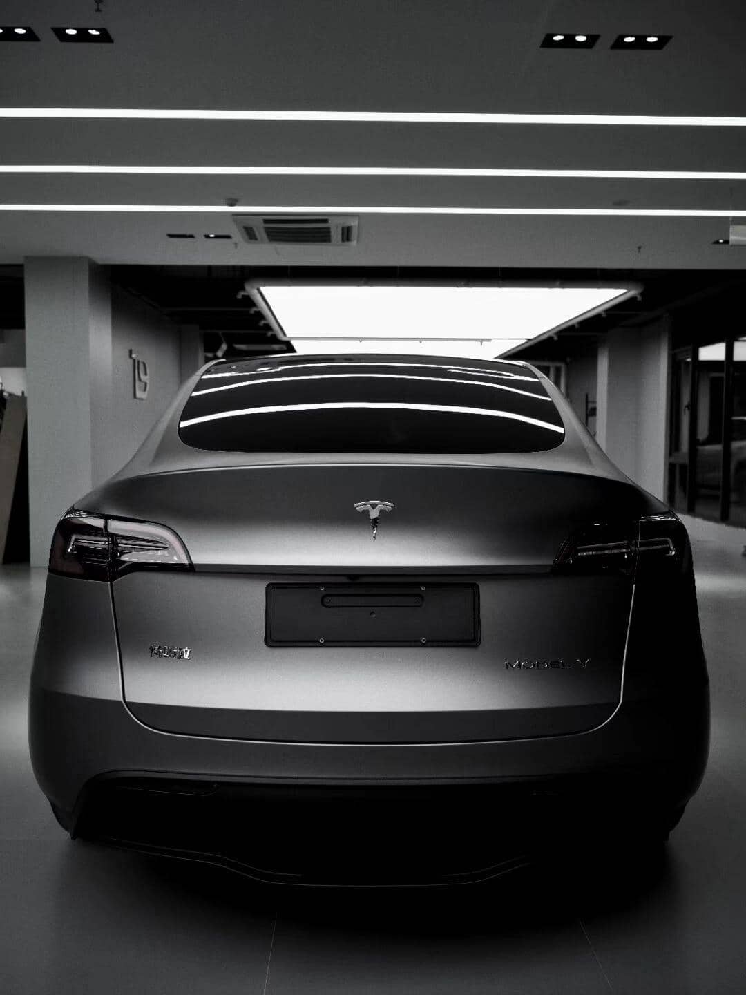 Rear view of a matte black Tesla Model X parked indoors under bright ceiling lights