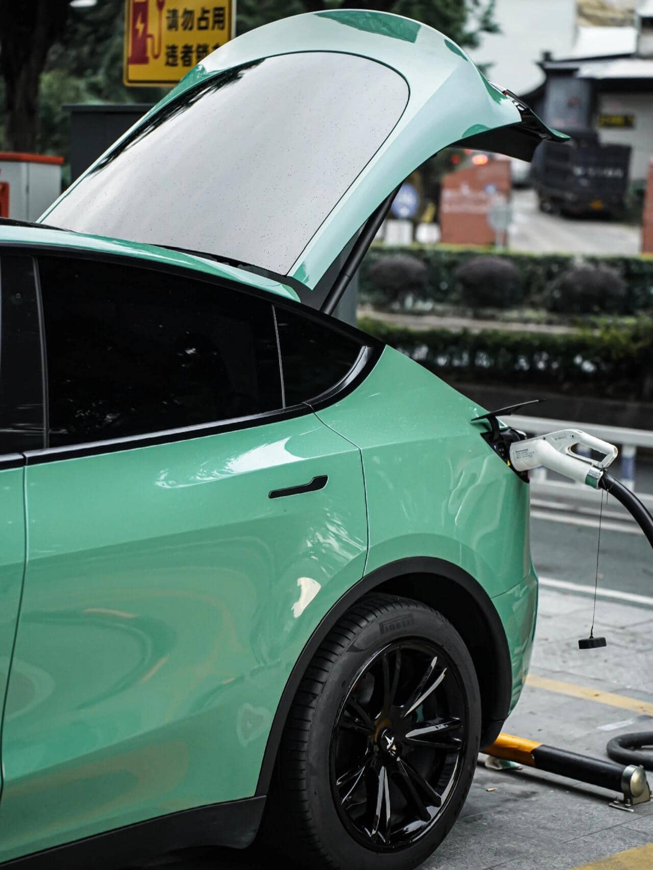 Pre-cut Tesla Vinyl Wrap Kit applied on green Tesla Model Y charging at station with open trunk