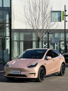 Pink Tesla Model Y wrapped using a Pre-cut Tesla Wrap Kit by WrapBug parked in front of a modern building