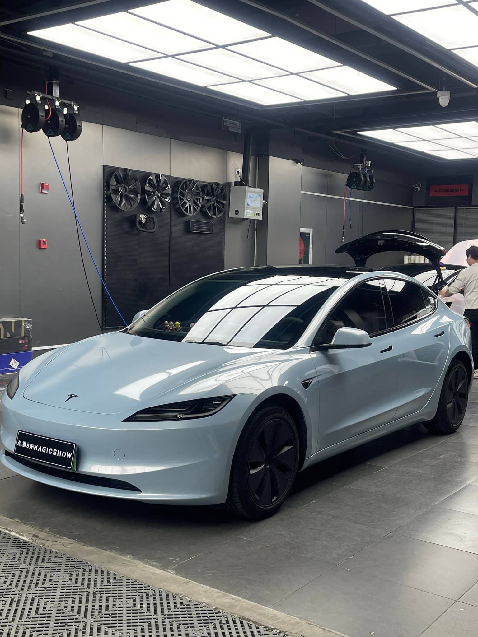 White Tesla Model 3 parked in a garage with reflective ceiling lights and black alloy wheels