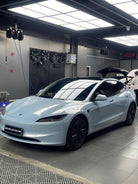 White Tesla Model 3 parked in a garage with reflective ceiling lights and black alloy wheels