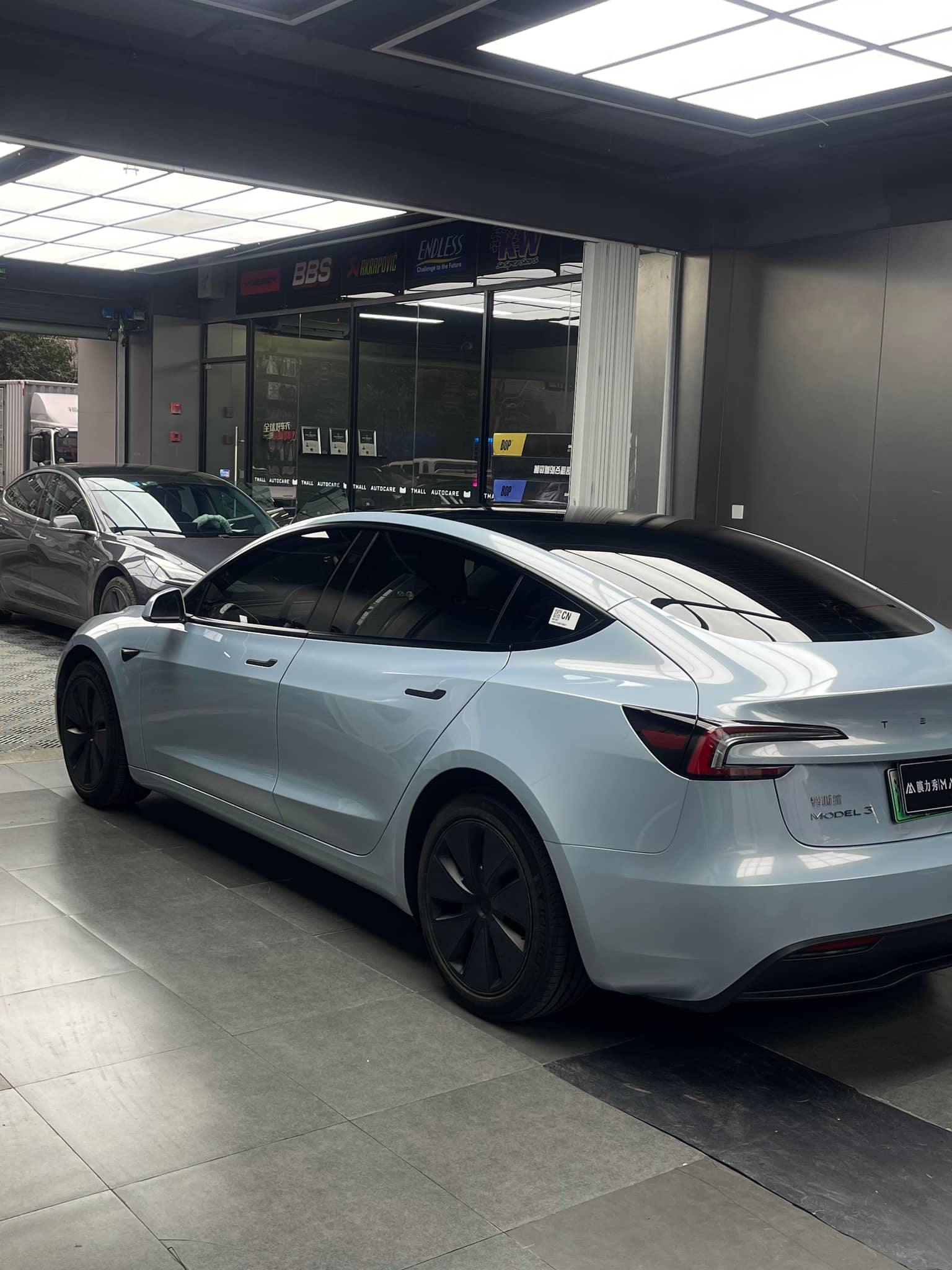 Silver Tesla Model 3 electric car parked indoors with tinted windows and black wheel covers