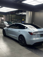 Silver Tesla Model 3 electric car parked indoors with tinted windows and black wheel covers