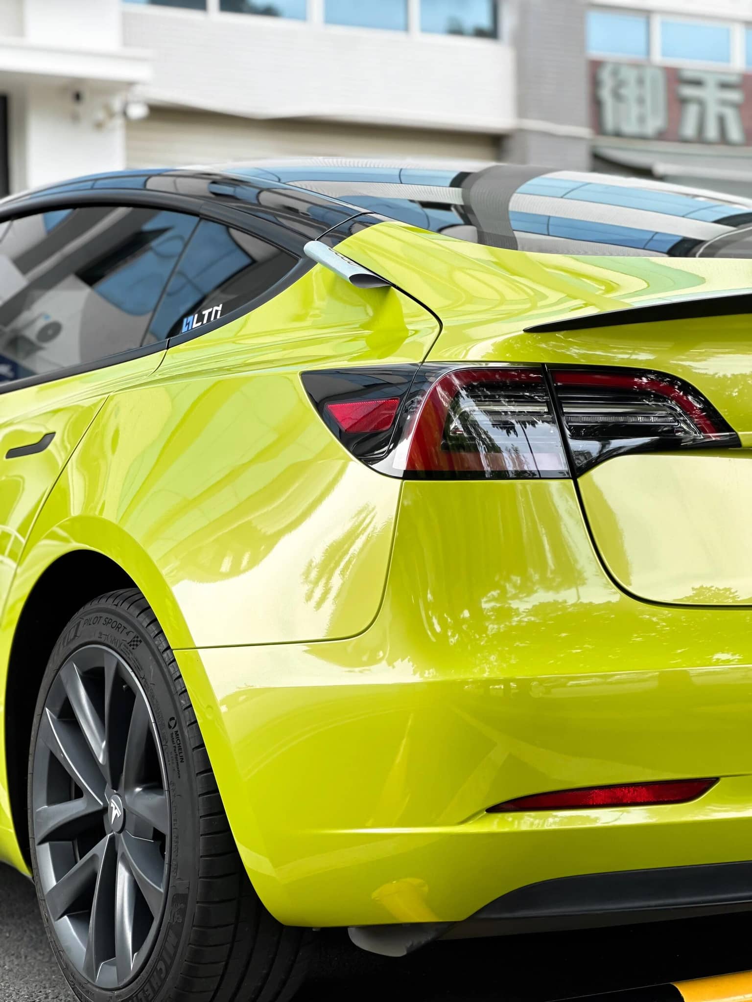 Bright yellow Tesla Model 3 wrapped with pre-cut Tesla vinyl wrap kit by WrapBug showing rear side view