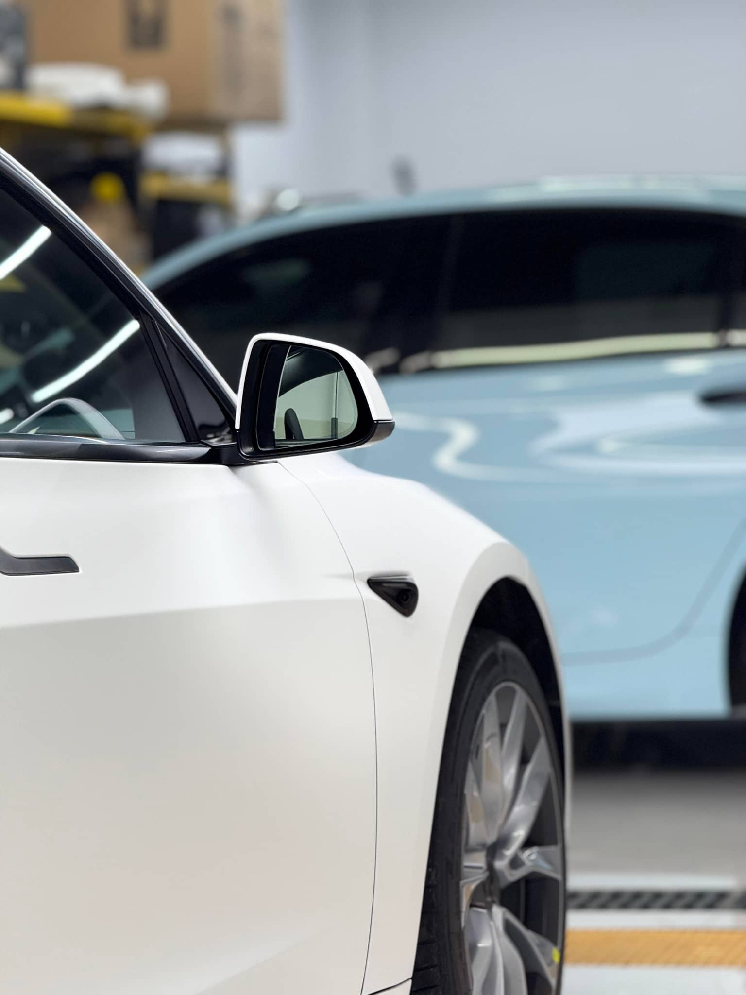 White Tesla with Pre-cut Tesla Vinyl Wrap Kit applied, focusing on side mirror and front wheel in a garage