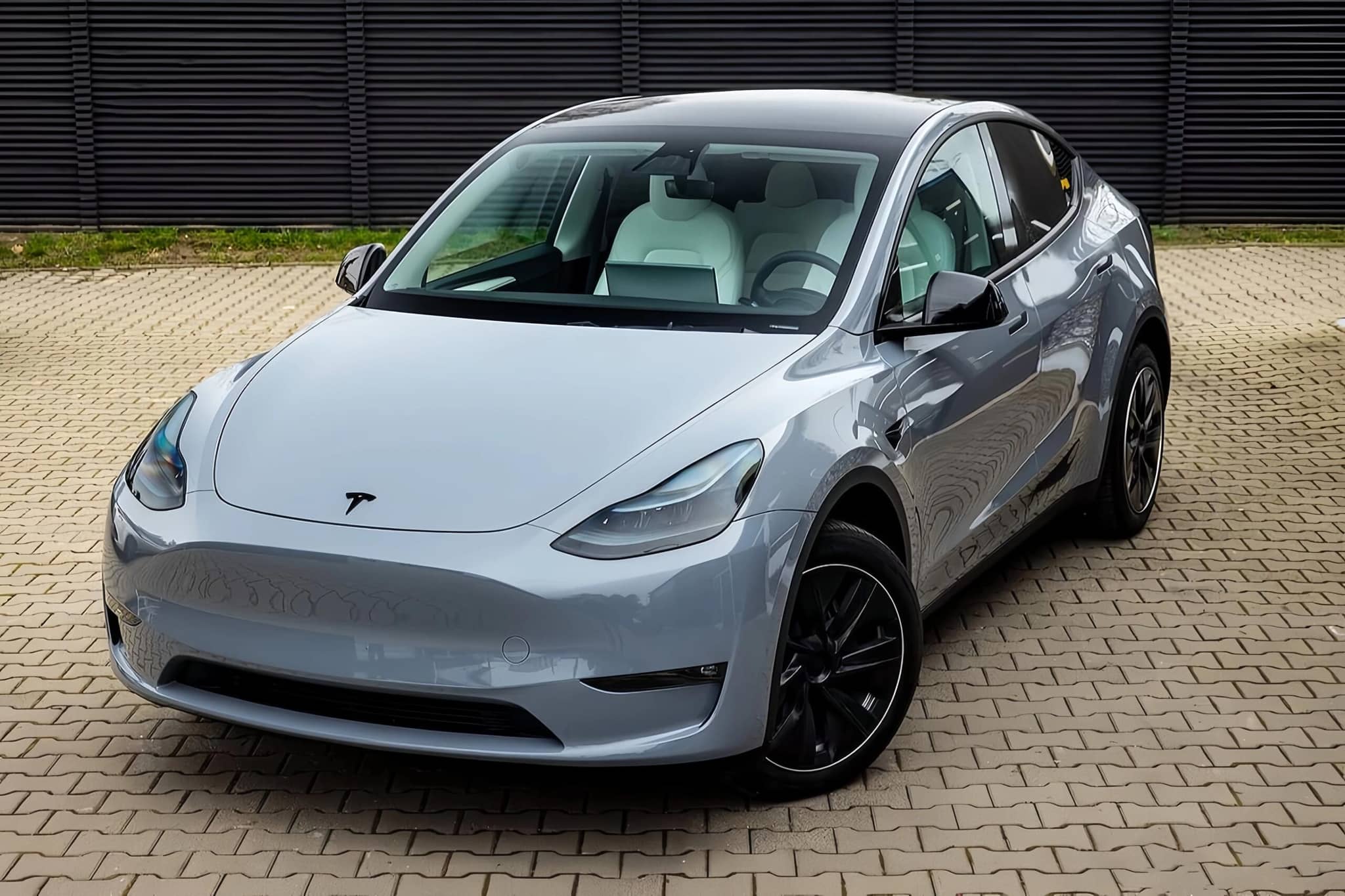 Silver Tesla Model Y electric SUV parked on tiled ground with black alloy wheels