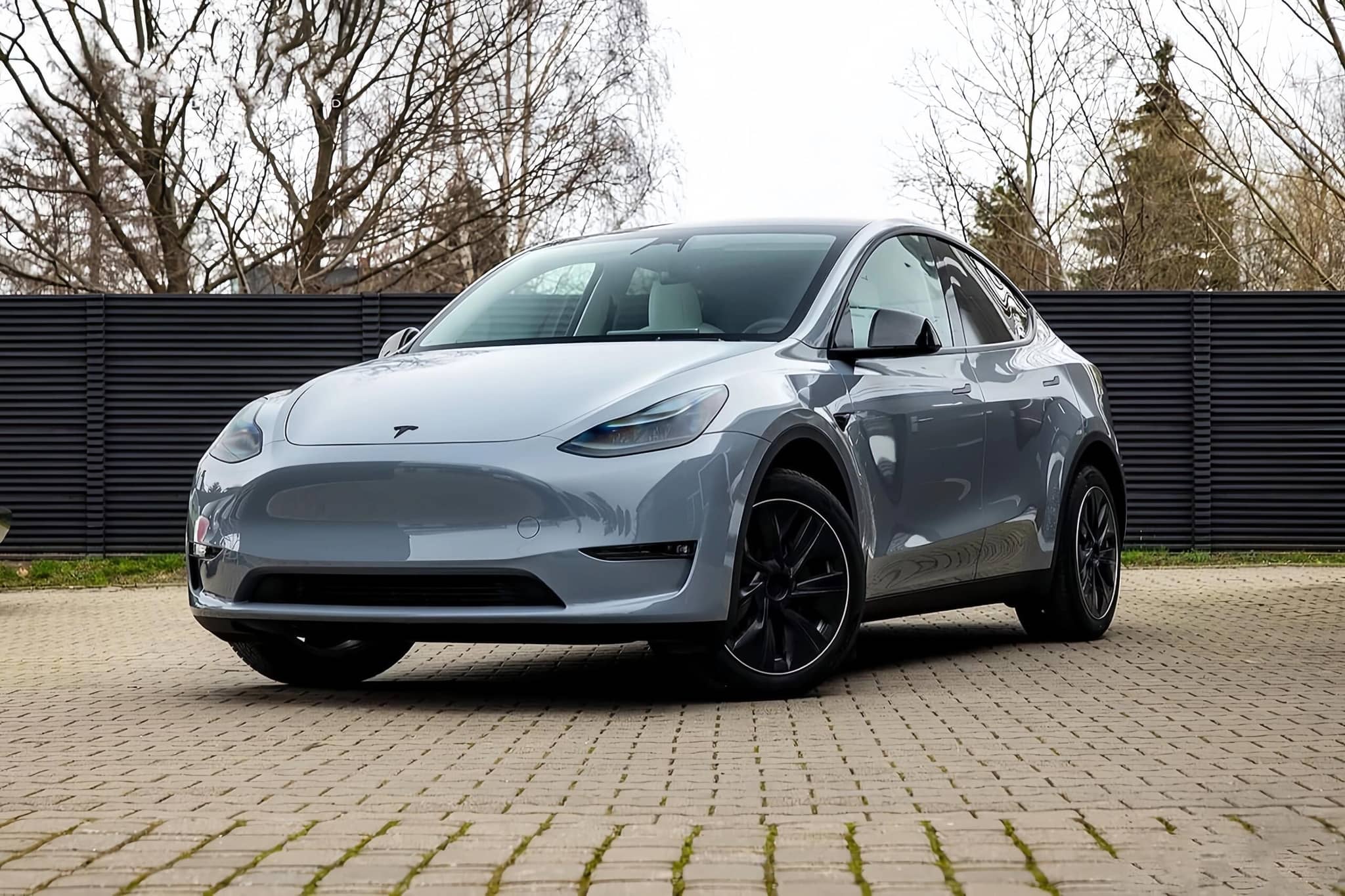 Silver Tesla Model Y electric SUV parked on a paved driveway with black wheels