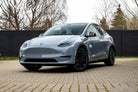 Silver Tesla Model Y electric SUV parked on a paved driveway with black wheels