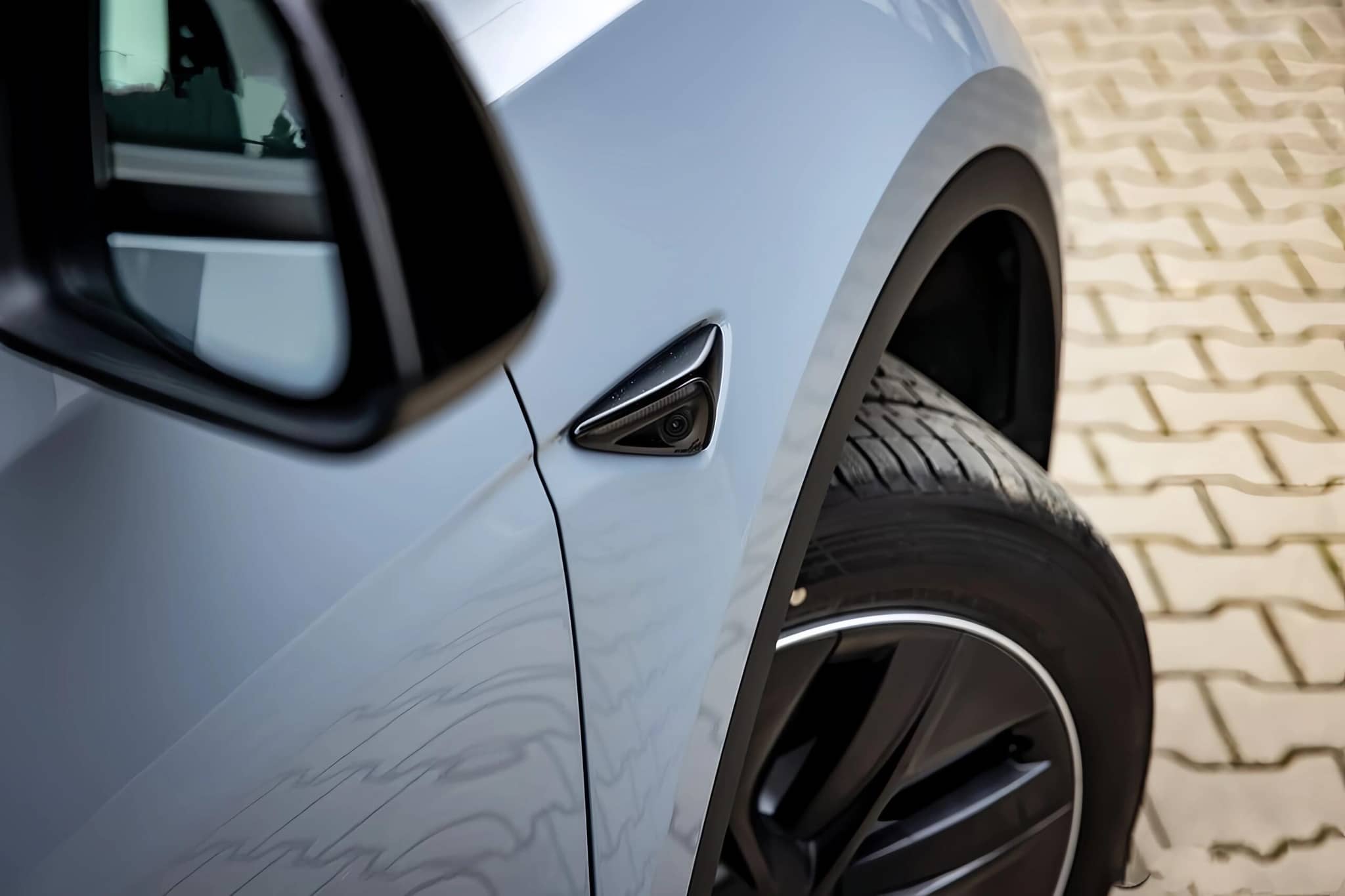 Close-up of light blue car's front wheel and side mirror with WrapBug paint protection film applied