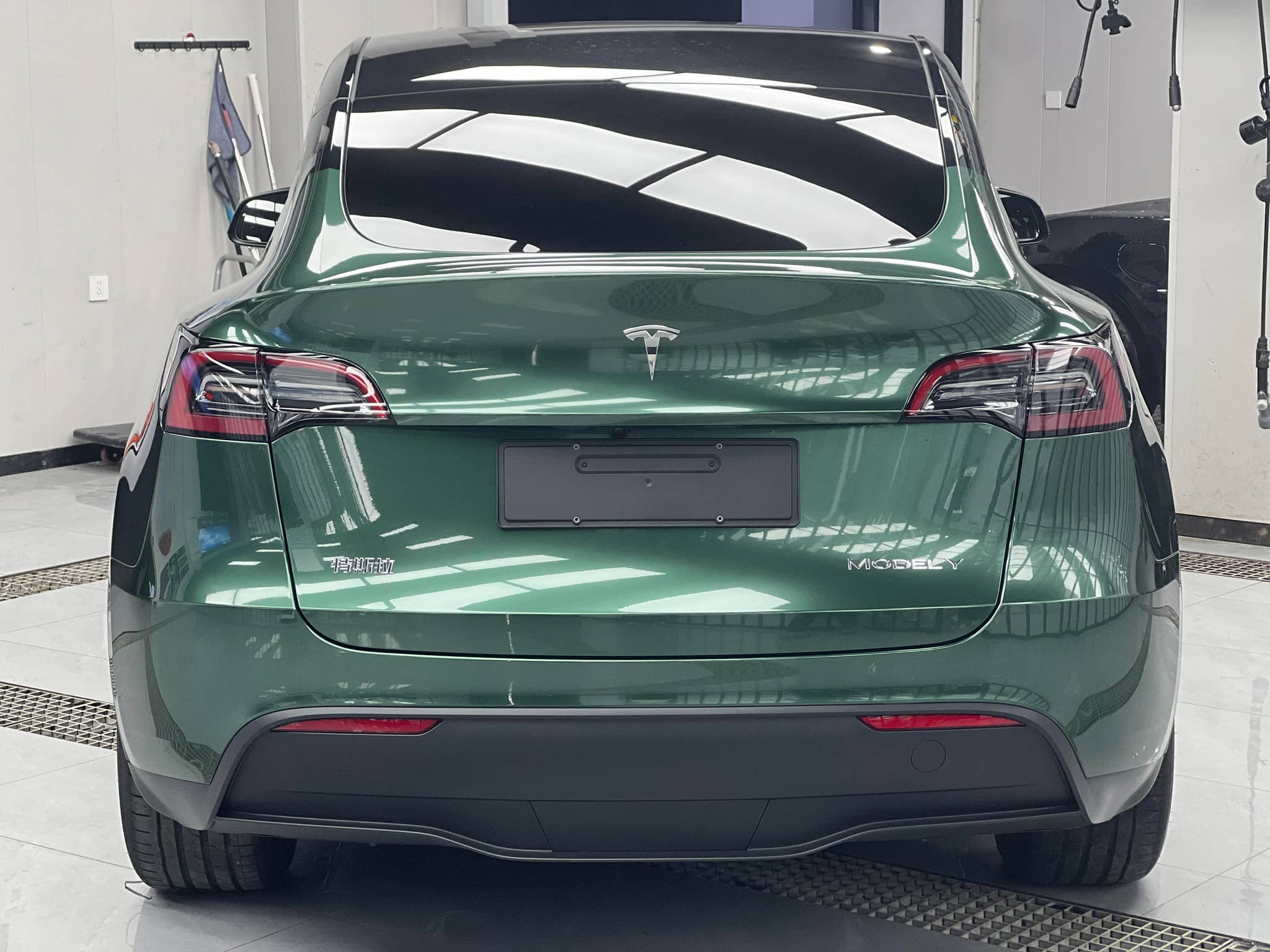 Green Tesla Model Y rear view wrapped with a Pre-cut Tesla Wrap Kit from WrapBug in a garage